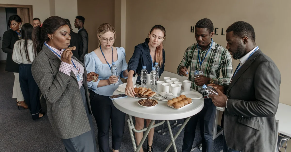 Asistentes a un evento conversando y sirviéndose un refrigerio alrededor de una mesa